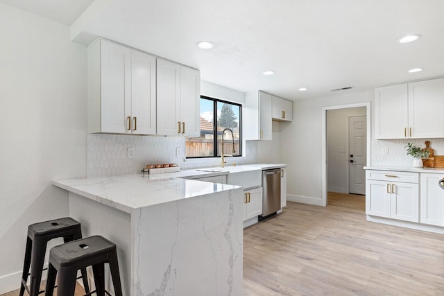 kitchen with a kitchen bar, white cabinetry, light wood-type flooring, kitchen peninsula, and light stone countertops