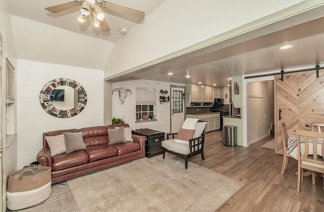 living room with vaulted ceiling, a barn door, ceiling fan, and light wood-type flooring