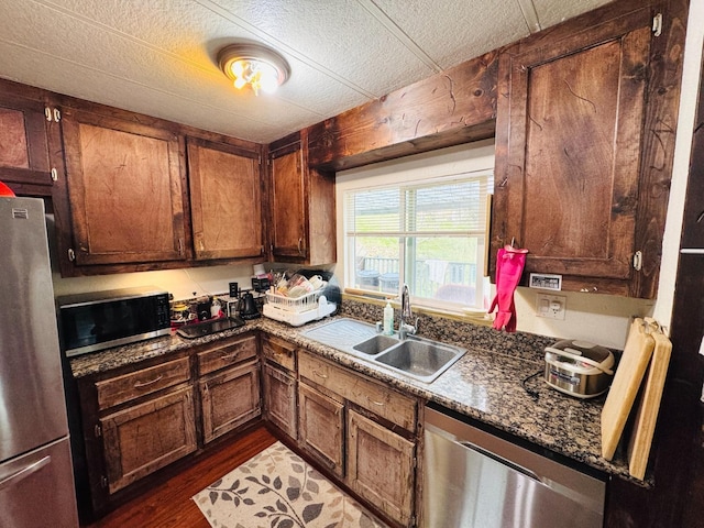 kitchen featuring sink, dark wood-type flooring, stainless steel appliances, a textured ceiling, and dark stone counters