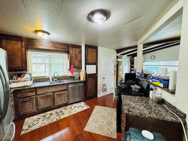 kitchen with appliances with stainless steel finishes, vaulted ceiling with beams, sink, dark hardwood / wood-style flooring, and dark stone counters