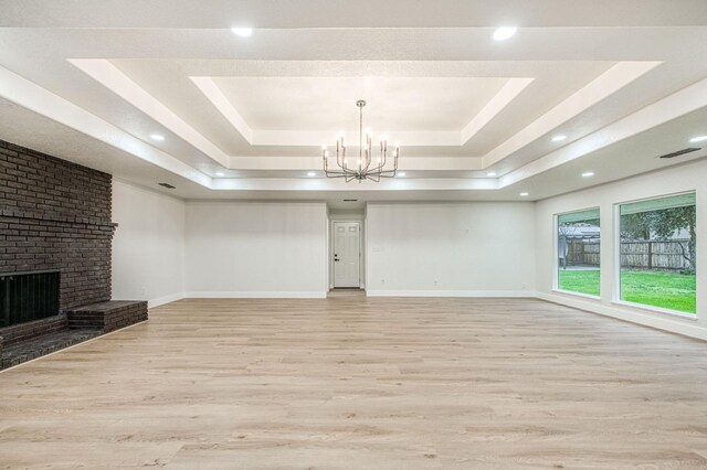 unfurnished living room featuring light hardwood / wood-style flooring, a fireplace, a raised ceiling, and an inviting chandelier