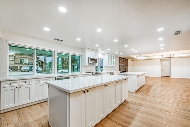 kitchen with stainless steel appliances, a center island, white cabinets, and light wood-type flooring