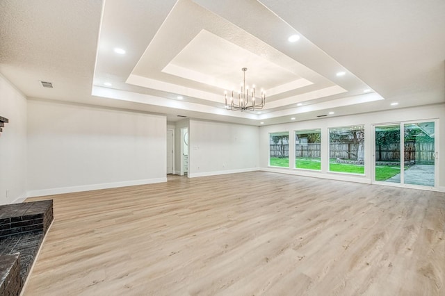 unfurnished living room featuring an inviting chandelier, light hardwood / wood-style floors, and a tray ceiling