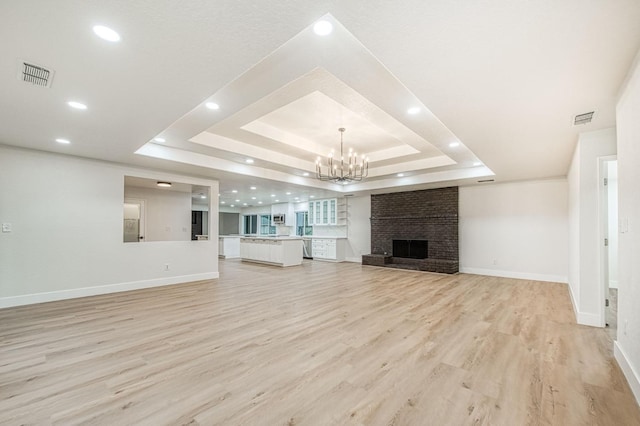 unfurnished living room featuring an inviting chandelier, a fireplace, a tray ceiling, and light hardwood / wood-style flooring