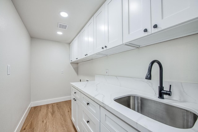 interior space with white cabinetry, sink, light stone counters, and light hardwood / wood-style flooring