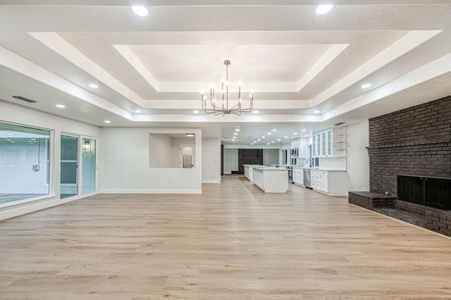 unfurnished living room featuring a raised ceiling, a brick fireplace, a chandelier, and light hardwood / wood-style floors