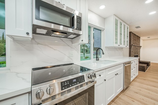 kitchen featuring sink, white cabinetry, stainless steel appliances, light stone countertops, and light wood-type flooring