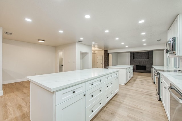 kitchen with a large island, light hardwood / wood-style flooring, stainless steel appliances, light stone counters, and white cabinets