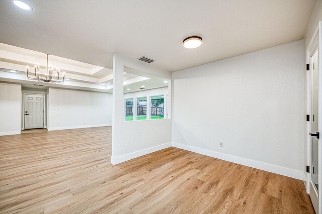 unfurnished room with an inviting chandelier, light hardwood / wood-style floors, and a tray ceiling