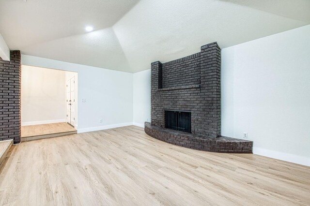 unfurnished living room featuring a fireplace, light hardwood / wood-style floors, and vaulted ceiling