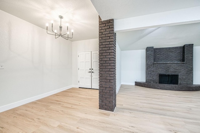 interior space with a brick fireplace, light hardwood / wood-style floors, a textured ceiling, and ornate columns