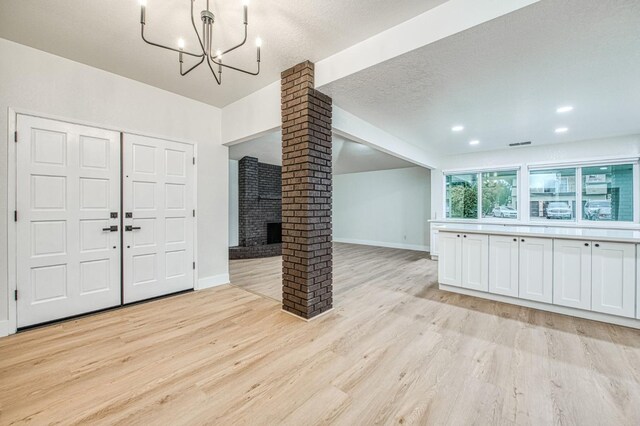 entrance foyer with a chandelier, decorative columns, a textured ceiling, and light wood-type flooring