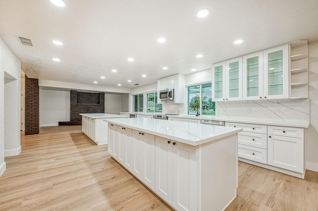 kitchen with a large island, stainless steel appliances, white cabinets, and light wood-type flooring