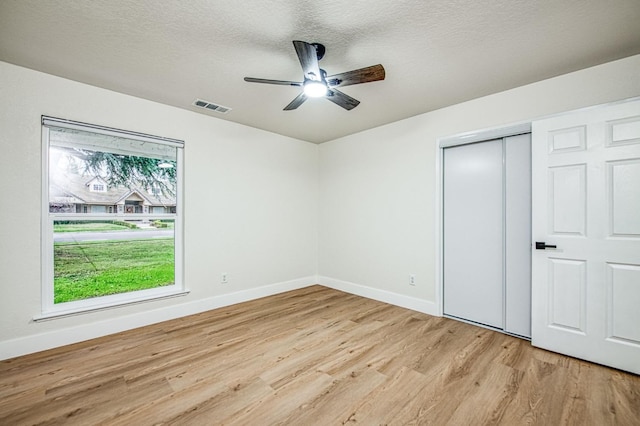 unfurnished bedroom with ceiling fan, a closet, a textured ceiling, and light wood-type flooring