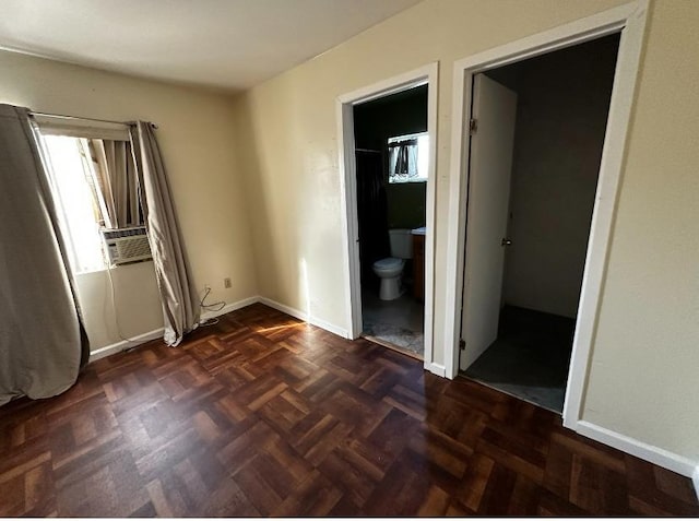 unfurnished bedroom with cooling unit, connected bathroom, and dark parquet floors