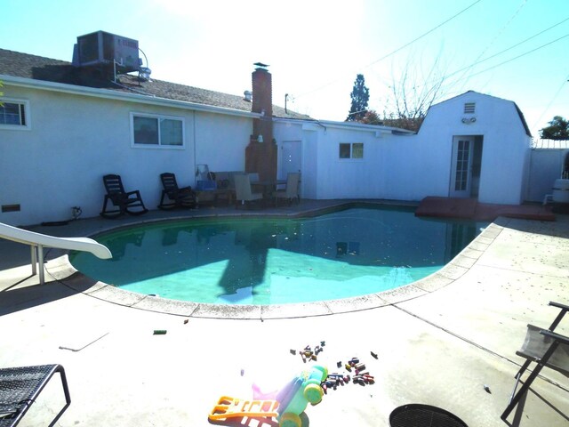 view of swimming pool with cooling unit, a water slide, and a patio area