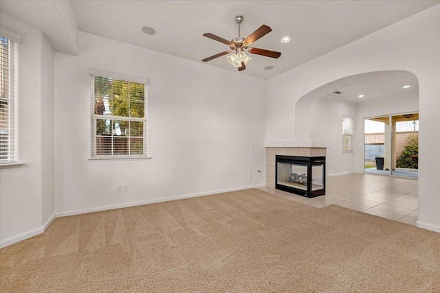 unfurnished living room featuring a tile fireplace, light carpet, and ceiling fan