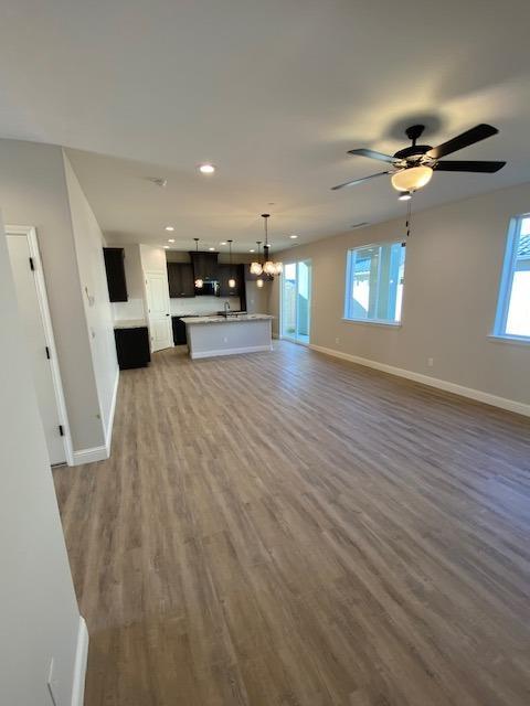 unfurnished living room with ceiling fan with notable chandelier and dark hardwood / wood-style flooring