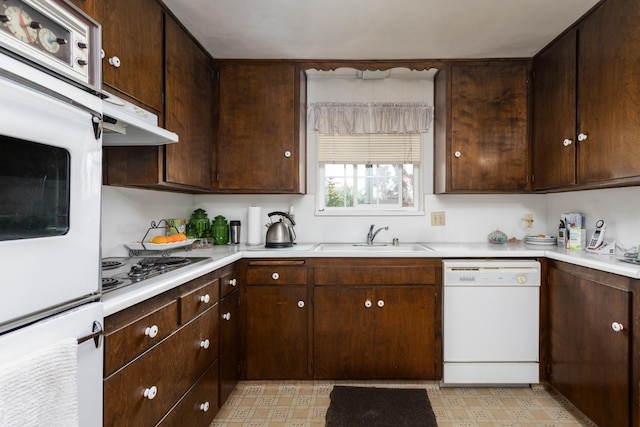 kitchen with a sink, white appliances, under cabinet range hood, and light floors