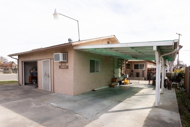 rear view of house with driveway, a wall mounted air conditioner, fence, and stucco siding