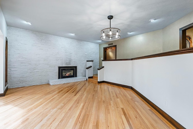 unfurnished living room with a stone fireplace, an inviting chandelier, and light hardwood / wood-style flooring