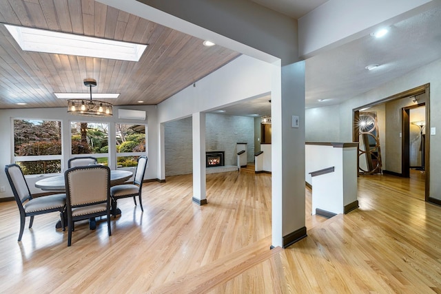 dining room with a wall mounted air conditioner, a fireplace, a skylight, light wood-type flooring, and an inviting chandelier