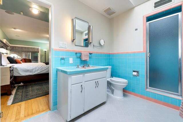 bathroom featuring tile patterned flooring, tile walls, vanity, toilet, and walk in shower