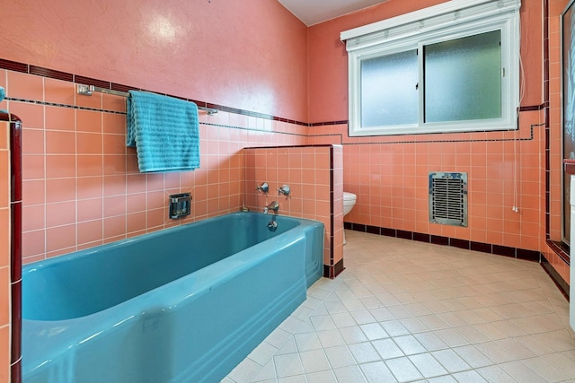 bathroom featuring heating unit, tile walls, a tub to relax in, toilet, and tile patterned floors