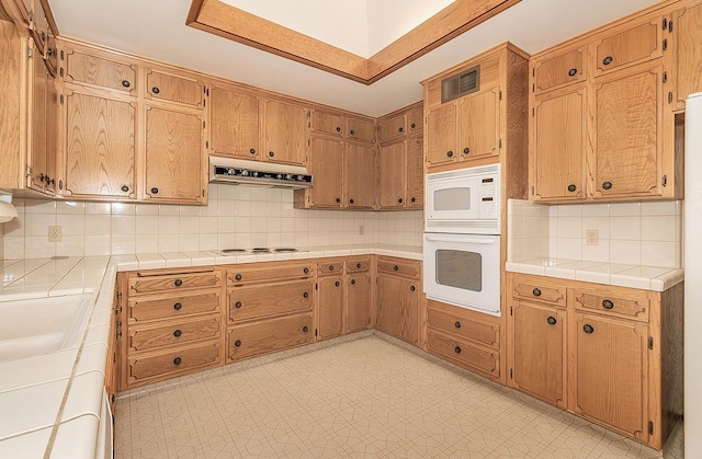 kitchen featuring tile countertops, white appliances, and decorative backsplash