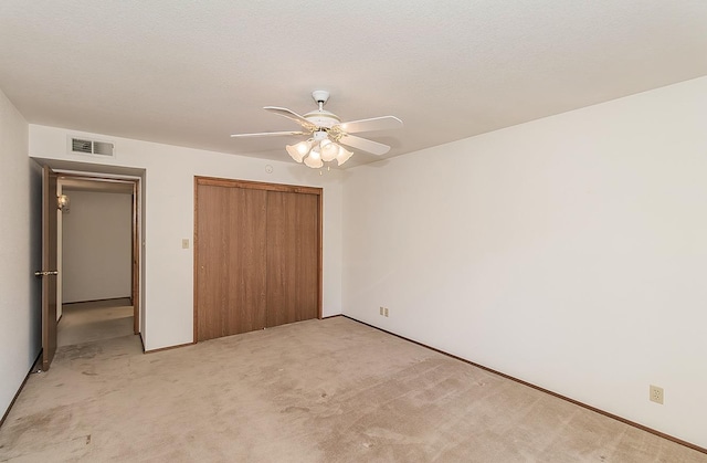 unfurnished bedroom featuring ceiling fan, light colored carpet, a closet, and a textured ceiling