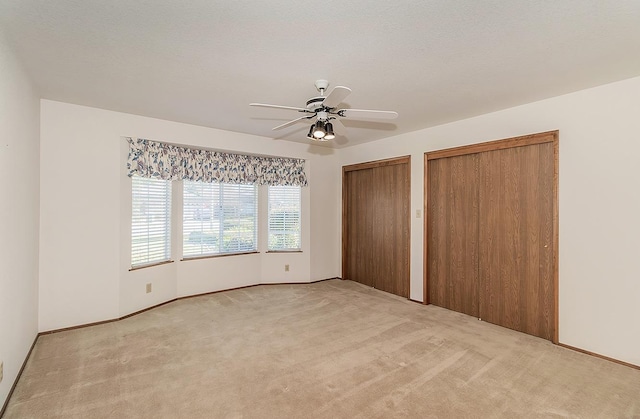 unfurnished bedroom featuring two closets, light colored carpet, ceiling fan, and a textured ceiling