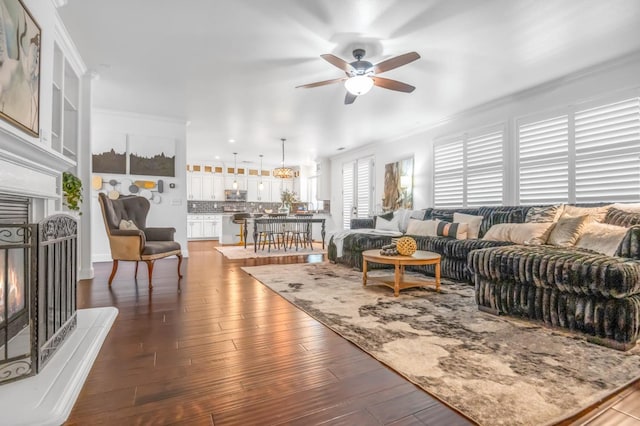 living area featuring crown molding, wood finished floors, a lit fireplace, and ceiling fan