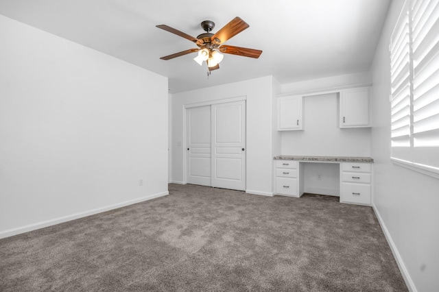 unfurnished office with ceiling fan, baseboards, built in study area, and carpet