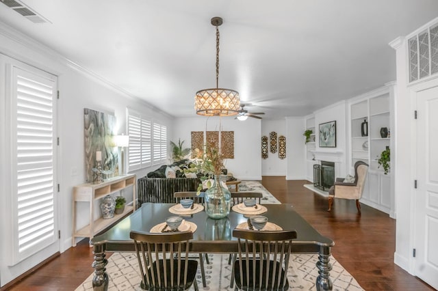 dining space with visible vents, a ceiling fan, a glass covered fireplace, dark wood finished floors, and crown molding