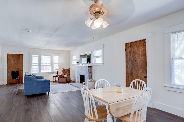 dining space featuring ceiling fan, a brick fireplace, and dark hardwood / wood-style flooring