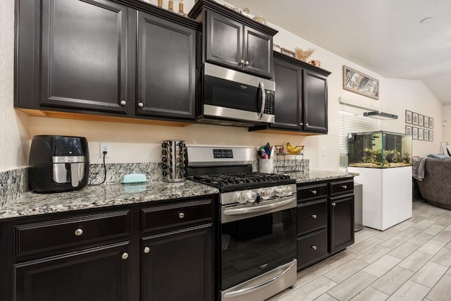 kitchen featuring stainless steel appliances, lofted ceiling, and light stone counters