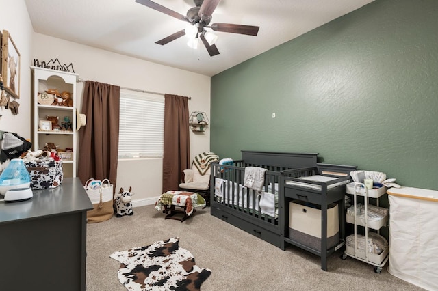 carpeted bedroom featuring a nursery area and ceiling fan