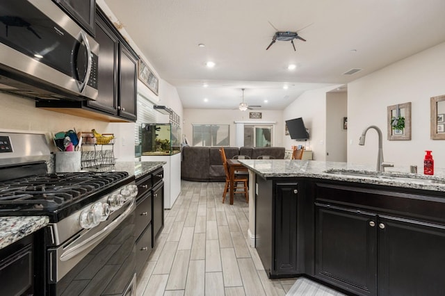 kitchen featuring stainless steel appliances, ceiling fan, sink, and light stone counters