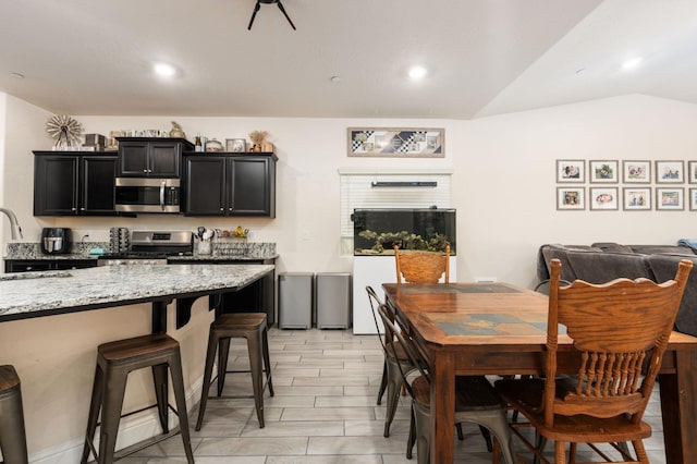 kitchen with light stone counters, a breakfast bar area, stainless steel appliances, and lofted ceiling