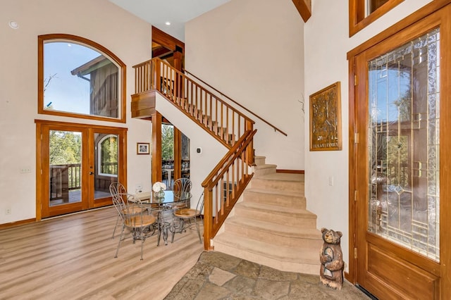 stairs with a towering ceiling, hardwood / wood-style floors, and french doors