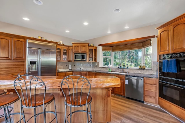 kitchen with built in appliances, backsplash, light hardwood / wood-style floors, and a center island