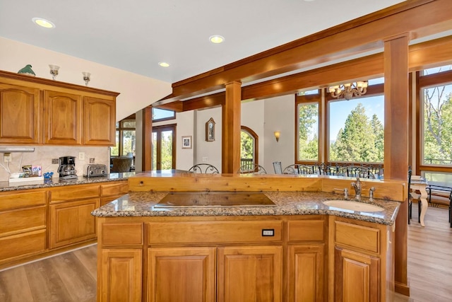 kitchen with sink, light stone counters, light hardwood / wood-style floors, a kitchen island, and black electric cooktop