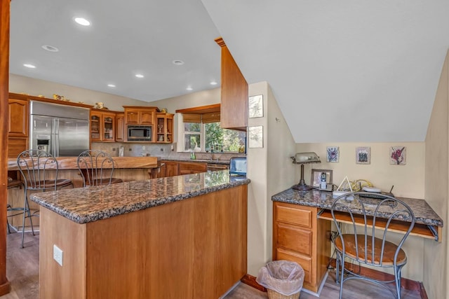 kitchen featuring vaulted ceiling, built in desk, dark stone counters, built in appliances, and kitchen peninsula