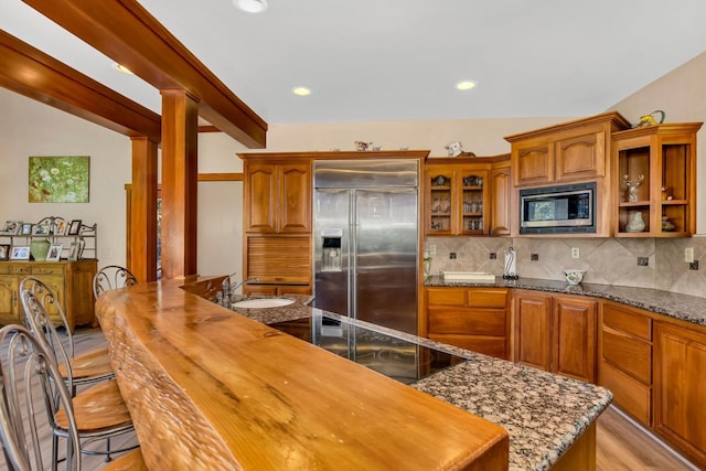 kitchen featuring built in appliances, sink, decorative backsplash, and dark stone countertops