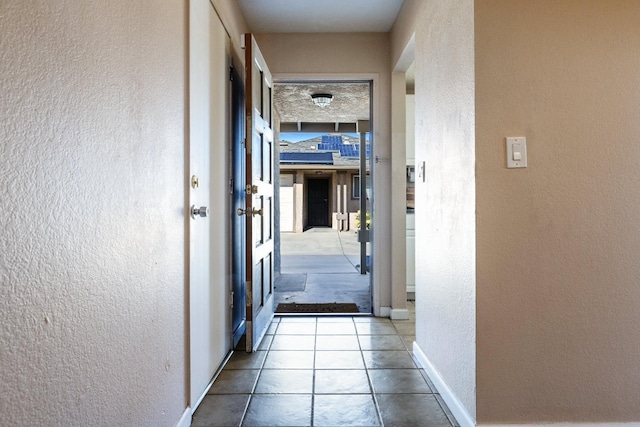 hallway featuring a textured wall, tile patterned floors, and baseboards