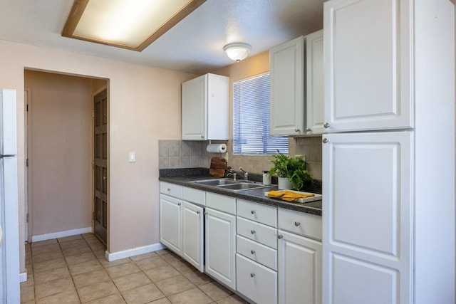 kitchen with dark countertops, decorative backsplash, white cabinets, a sink, and baseboards