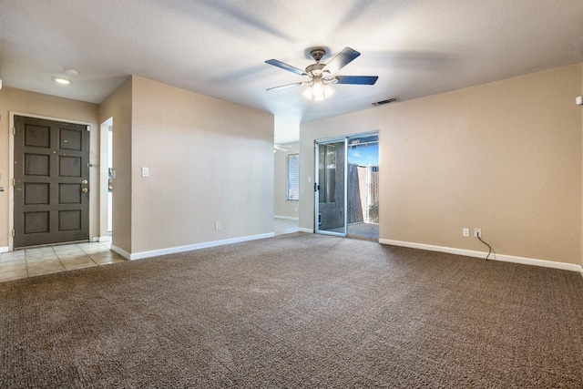 spare room with light carpet, light tile patterned floors, visible vents, baseboards, and ceiling fan