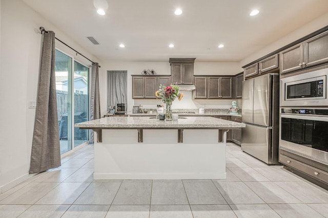 kitchen with stainless steel appliances, a kitchen island with sink, light stone counters, and a breakfast bar