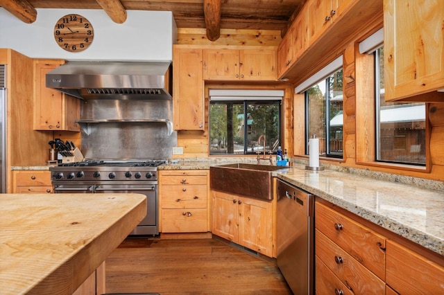 kitchen with appliances with stainless steel finishes, sink, dark hardwood / wood-style flooring, light stone counters, and wall chimney exhaust hood