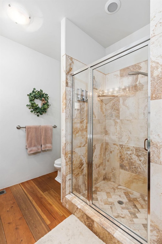 bathroom with toilet, a shower with door, and hardwood / wood-style floors